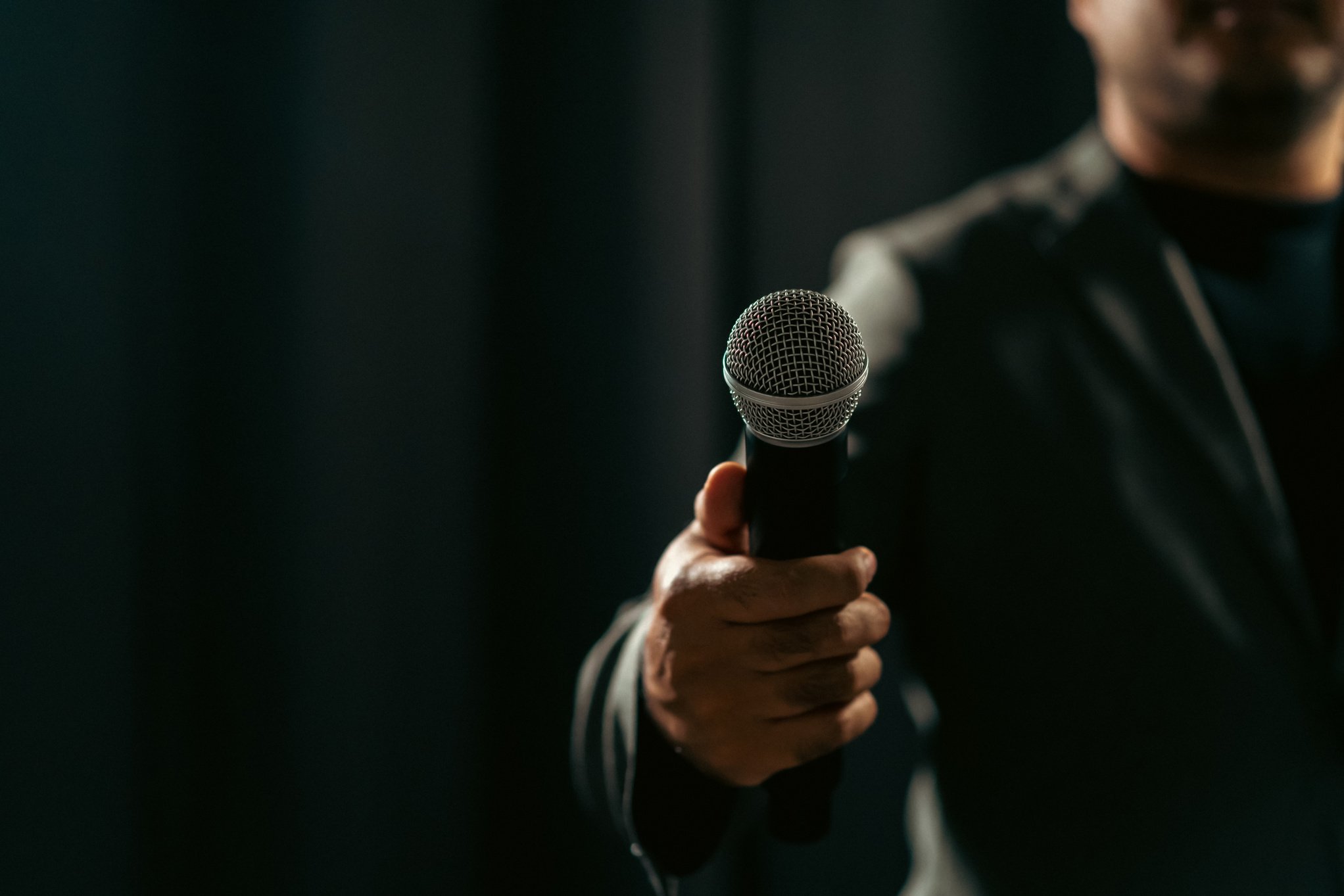 Confident successful speaker man talking on stage with spotlight strike through the darkness at corporate business event. Public speaker giving talk at conference hall. Stand up comedian.